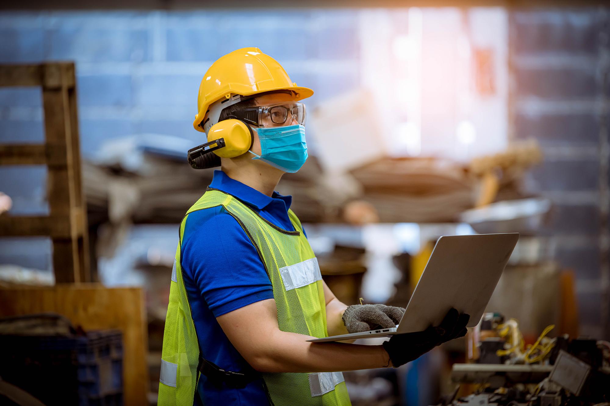 Engineer in personal protective equipment using a laptop on a construction site.