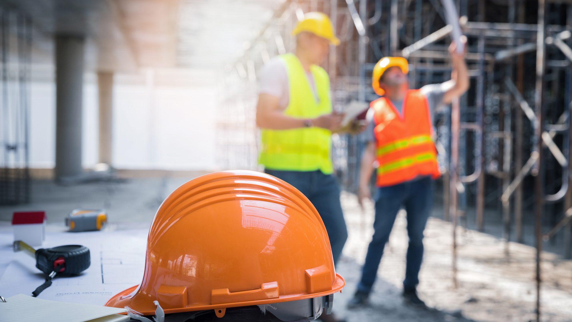 An orange helmet cap with two males looking at a plan. 