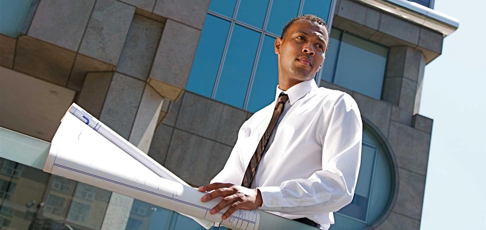 An African male in front of a construction building with blue prints. 